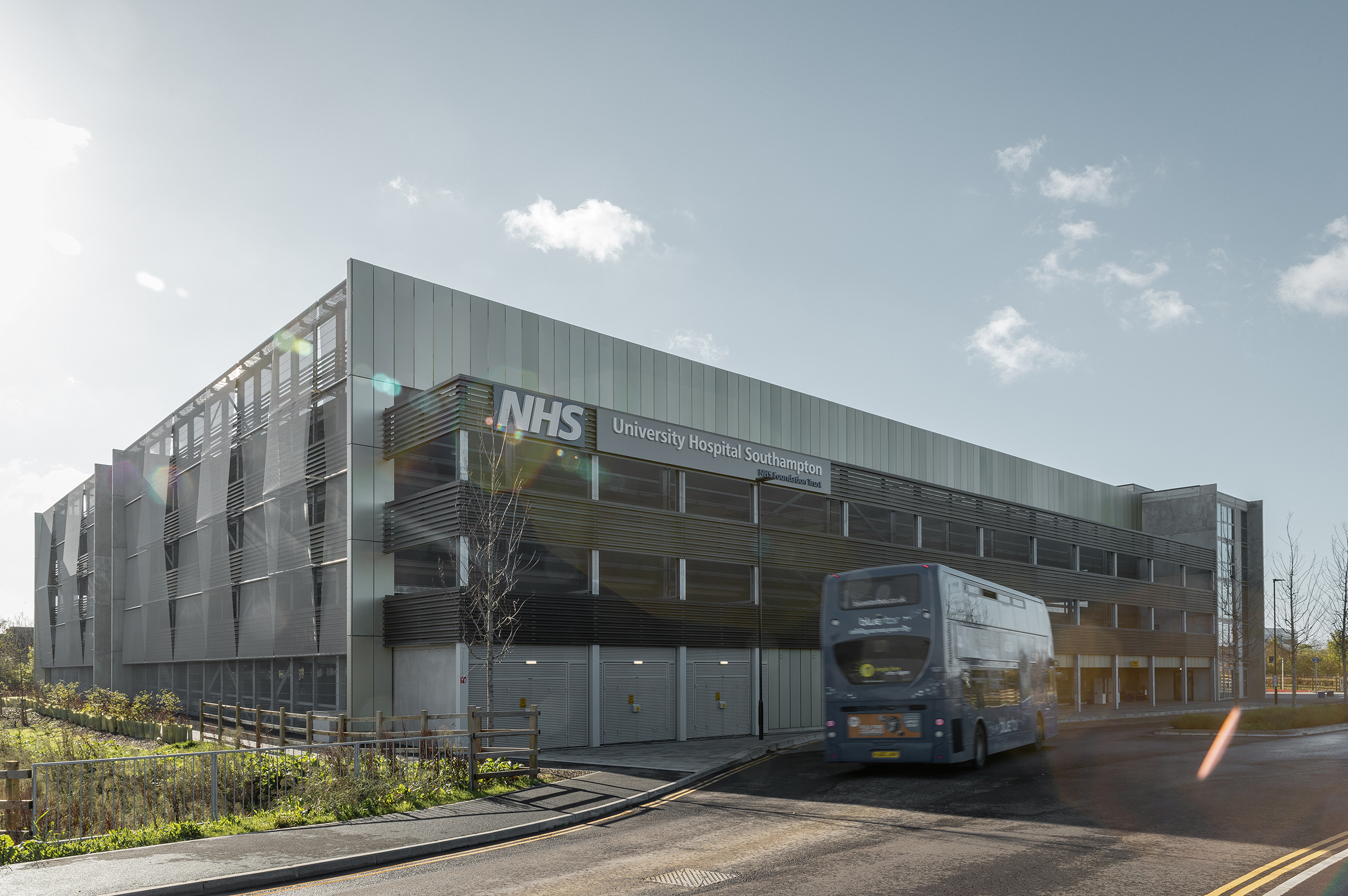Modernes mehrstöckiges Parkhaus des University Hospital Southampton mit seitlichen Lamellen, davor eine vorbeifahrende Linienbusse und hellem Tageslicht.