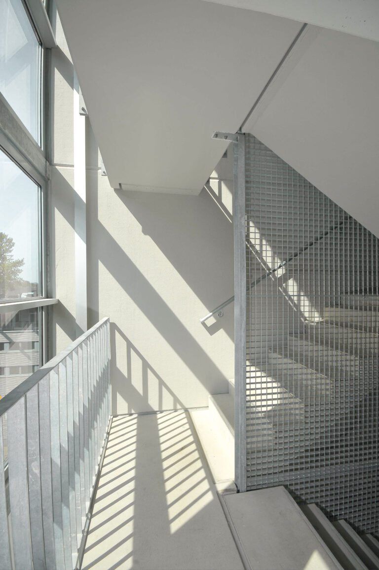 Treppenraum mit Tageslichteinfall, Betonflächen und Gitterelementen als Absturzsicherung.