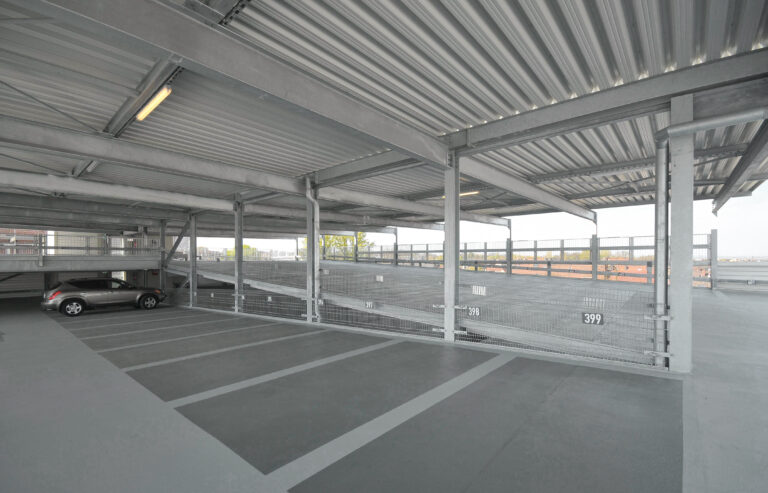 Parkebene mit Stellplätzen, Fahrgasse und offenem Stahltragwerk mit Absturzsicherung.
