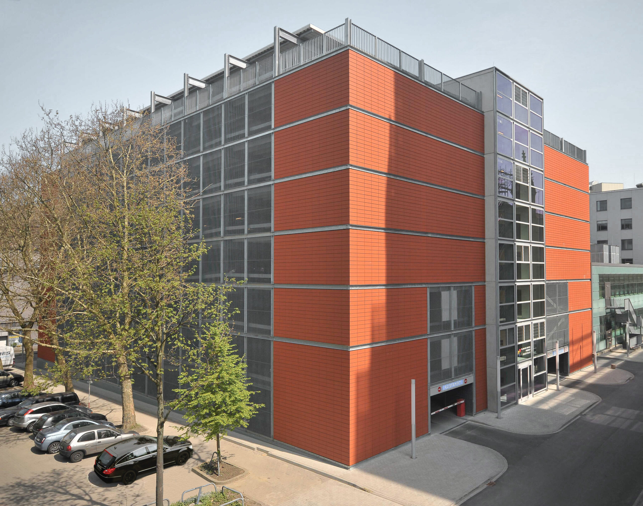 Außenansicht eines Parkhauses mit Kassettenfassade, Treppenhausturm und städtischem Umfeld.