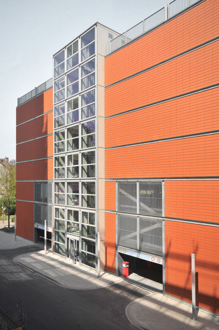 Außenansicht eines Parkhauses mit orangefarbener Kassettenfassade und verglastem Treppenhaus.