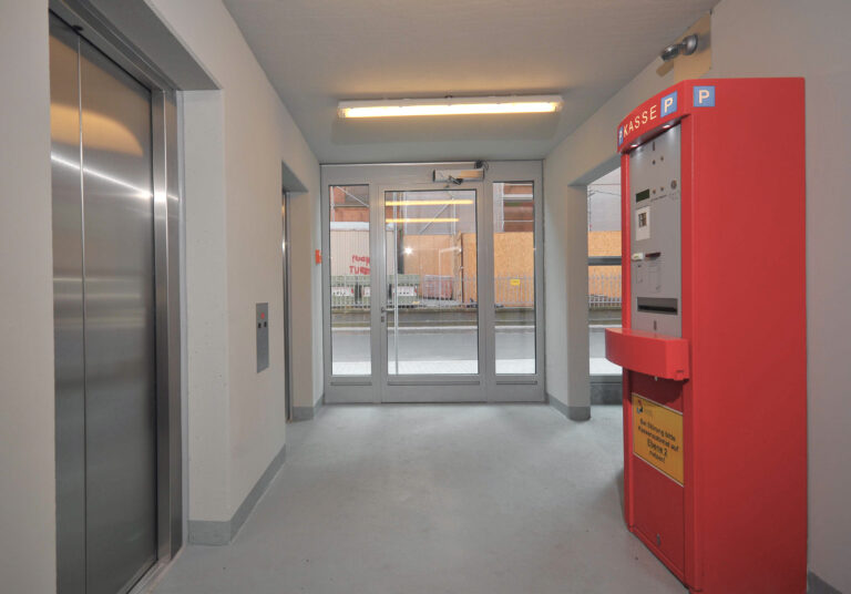 Eingangsbereich mit Aufzug und Kassenautomat innerhalb eines Parkhauses.