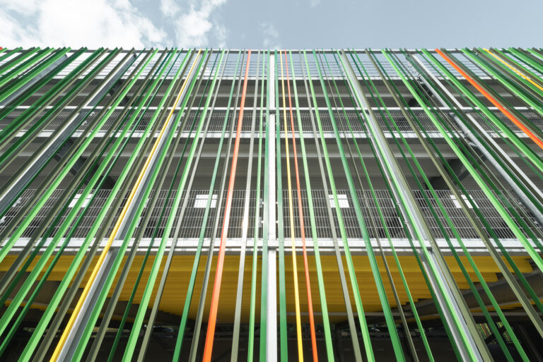 Detailansicht der Fassade mit vertikalen grünen, gelben und orangefarbenen Lamellen vor den Parkebenen.