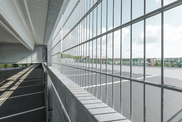 Blick durch ein Metallgitter auf das obere Parkdeck mit freier Stellfläche und umlaufender Absturzsicherung.