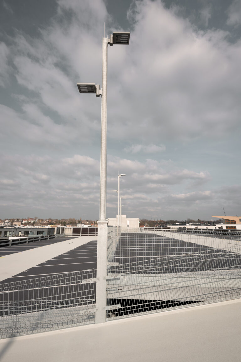 Beleuchteter Parkplatz auf dem obersten Parkdeck mit hohen LED-Lichtmasten und Stadtpanorama im Hintergrund.