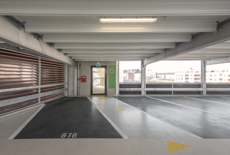 Parkdeck mit klar markierten Stellplätzen und Ebenenkennzeichnung „6“ sowie Blick auf Wohnbebauung.