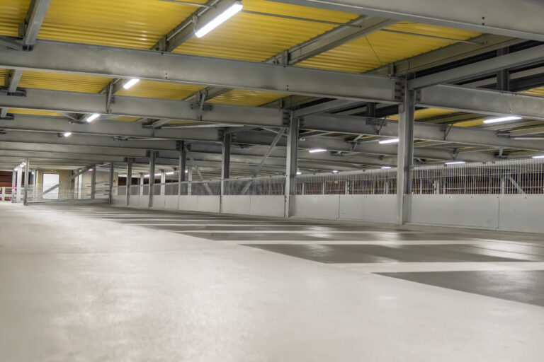 Parkdeck mit Stahlkonstruktion, Beleuchtung und markierten Stellplätzen.