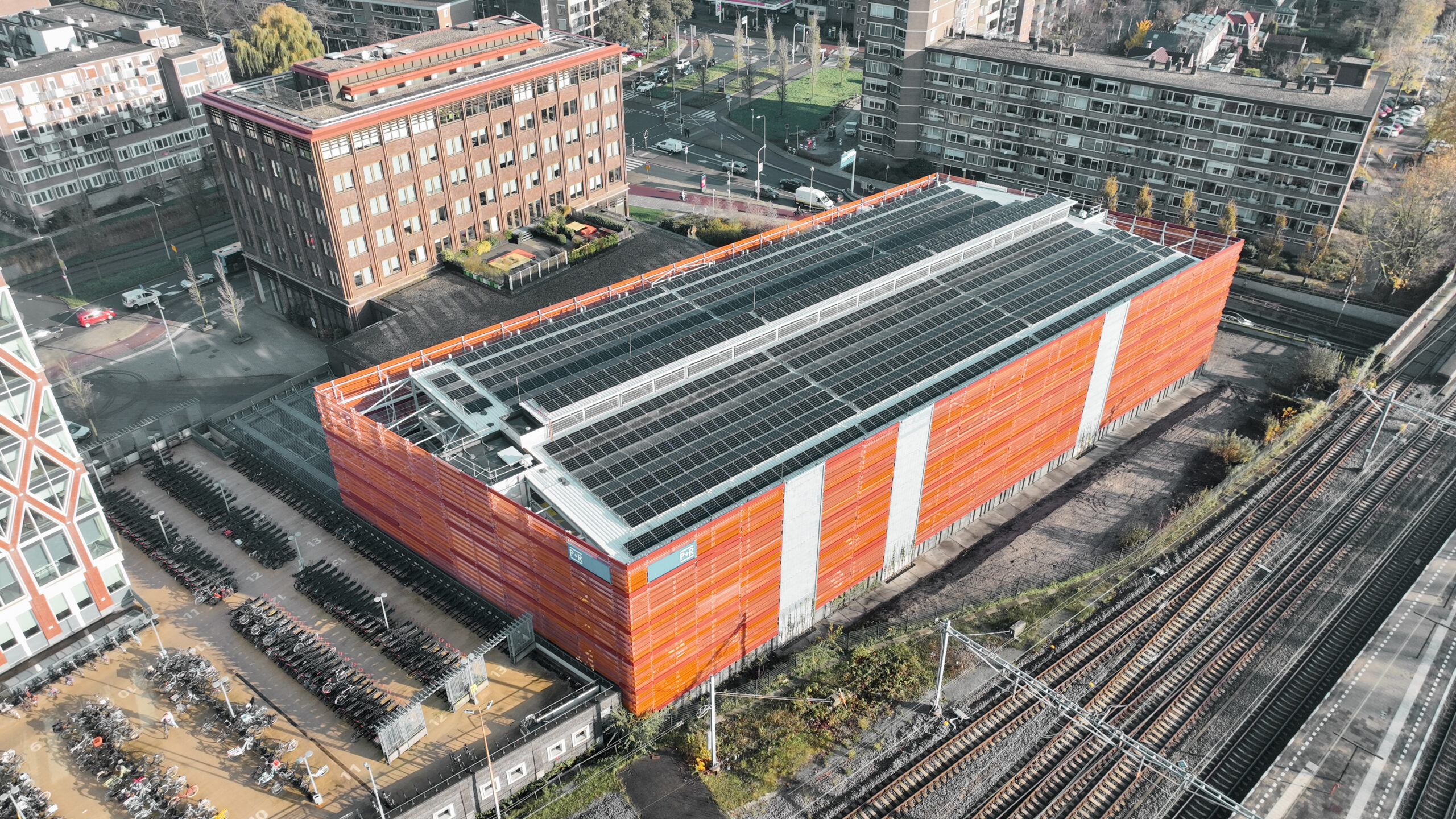 Luftaufnahme des P+R-Parkhauses Gouda mit Photovoltaikanlage auf dem Dach und Fahrradparkplätzen am Bahnhof.