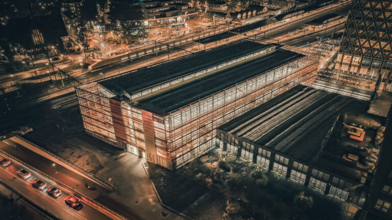 Luftaufnahme des beleuchteten Parkhauses bei Nacht am Bahnhof.