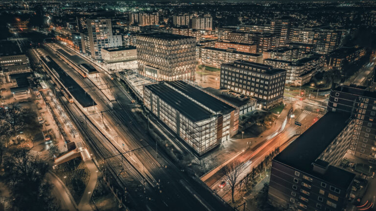 Luftaufnahme des beleuchteten P+R-Parkhauses Gouda am Bahnhof im nächtlichen Stadtbild.