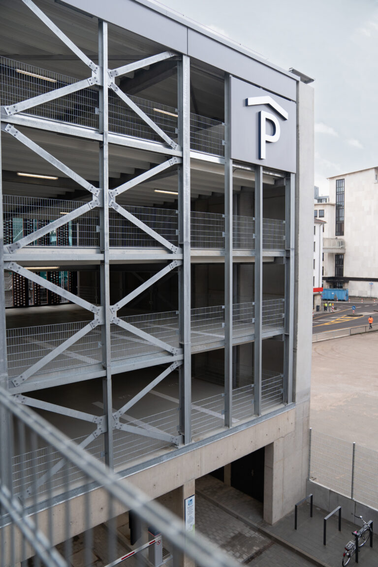 Mehrstöckiges Parkhaus mit offenen Parkdecks, Metallgeländern und gut sichtbarem Parksymbol.
