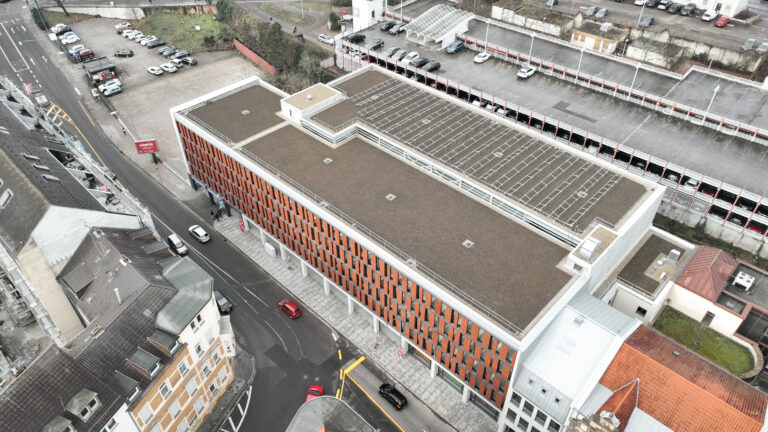 Luftaufnahme eines Parkhauses mit mehreren Parkebenen, begrüntem Dachbereich und direkter Anbindung an das urbane Umfeld.