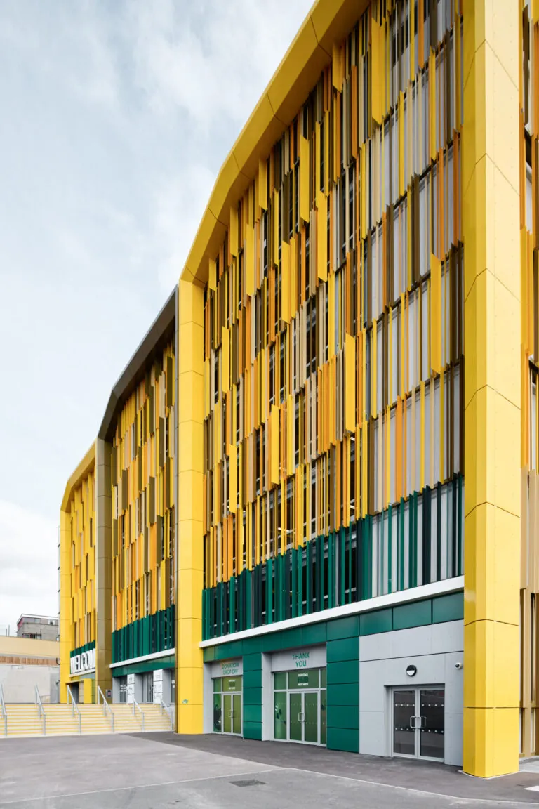 Modernes Parkhaus mit markanter gelber Fassadenstruktur und vertikalen Lamellen, aufgenommen aus der Eckperspektive vor bewölktem Himmel.