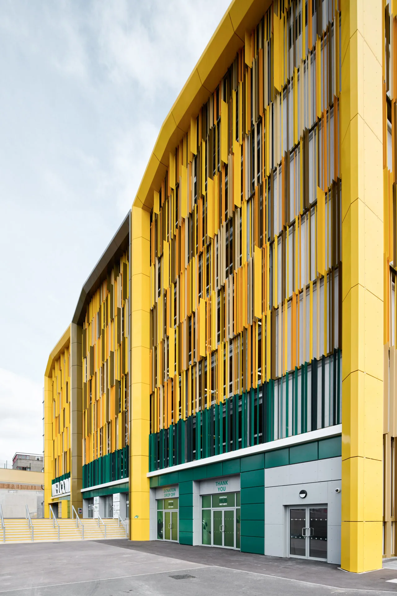 Modernes Parkhaus mit markanter gelber Fassadenstruktur und vertikalen Lamellen, aufgenommen aus der Eckperspektive vor bewölktem Himmel.