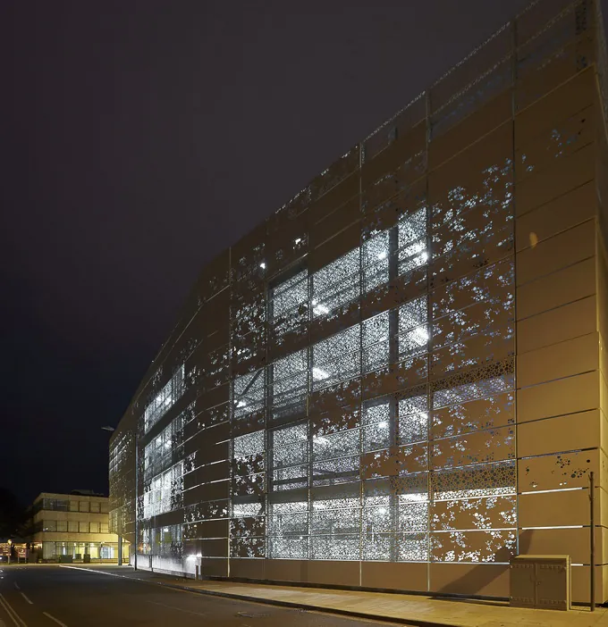 Nachts beleuchtetes Parkhaus mit perforierter Metallfassade und sichtbarer Innenstruktur.